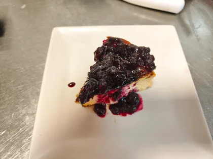 Porción de tarta de queso casera con mermelada de arándanos.